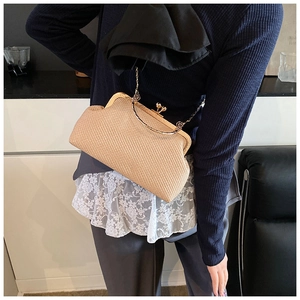 Detail of woven straw clutch bag with gold metal frame and ball clasp on shoulder