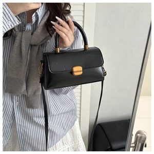 Detailed view of a black square leather handbag with gold clasp and elegant handle