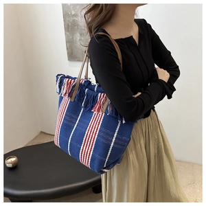 Detail view of large canvas tote bag with colorful stripes, tassels and leather strap