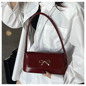 Gros plan du sac baguette rouge foncé brillant avec sa boucle élégante en nœud doré