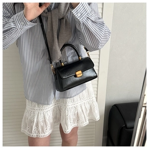 Detail of vintage black crossbody bag with gold lock buckle and top handle styling
