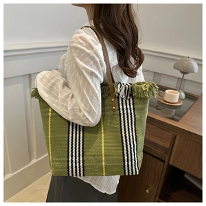 Close-up of green woven canvas tote with striped embroidery and brown leather handle