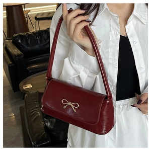 Détail du sac baguette rouge foncé avec boucle nœud dorée et cuir brillant poli
