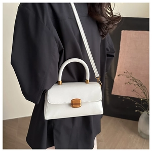 Close-up of white crossbody bag with vintage gold buckle on a black blazer outfit