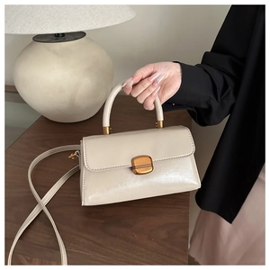 Close-up of beige leather handbag with gold metal clasp held by model in home setting