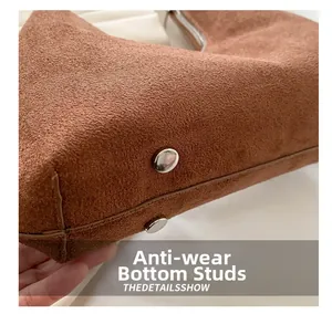Détail du fond d'un sac en daim marron montrant les pieds de protection et le zip argent