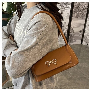 Détail d'un sac baguette en cuir PU marron avec boucle nœud doré sur un sweat-shirt gris
