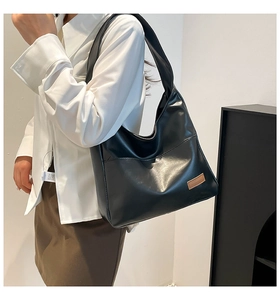 Minimalist black PU leather tote bag shown on shoulder in a stylish indoor setting