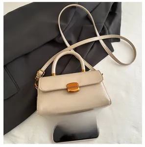 Detail of a cream crossbody bag with a gold oval metal clasp on a textured fabric