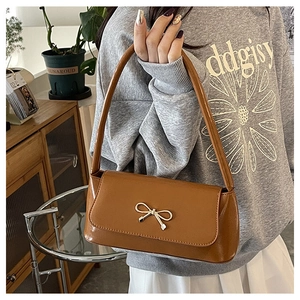 Gros plan du sac baguette en cuir marron avec boucle nœud dorée porté par un mannequin
