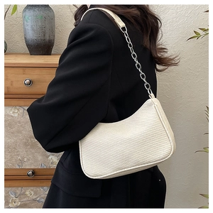 Detail of a beige woven underarm bag with a silver chain strap on a black blazer