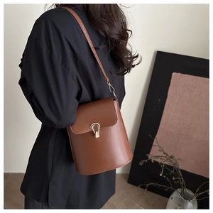 Detail of a brown leather bucket bag featuring a gold teardrop swivel lock and shoulder strap