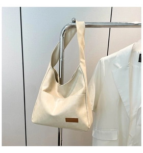 Detailed view of cream tote bag hanging by a blazer, showing minimalist hobo design