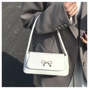 Détail du sac baguette blanc avec boucle dorée porté sur un blazer gris chic
