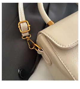 Detailed close-up of golden metal hooks and textured lychee leather on cream crossbody bag