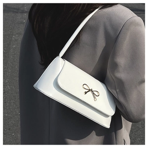 Détail d'un sac baguette en cuir verni blanc avec une boucle nœud en métal doré