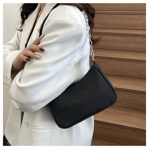 Detail of black textured underarm bag with industrial silver chain strap on white blazer