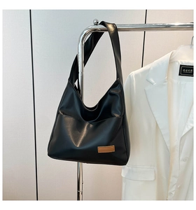 Close-up of black PU leather tote bag with brown patch hanging on a minimal steel rack