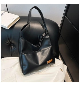 Macro detail of black PU leather tote bag with brown leather tag on textured sofa