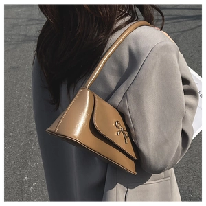 Détail du sac baguette en cuir verni kaki avec une boucle nœud doré sur un blazer gris