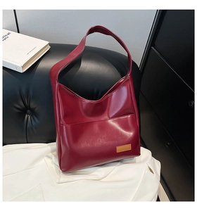 Detail of burgundy leather tote bag featuring a glossy finish and a minimalist brown logo patch