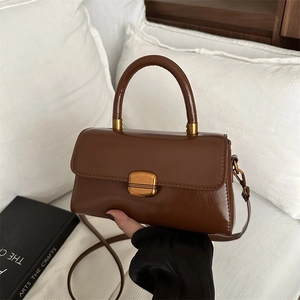 Retro brown leather square handbag with golden lock and strap in a cozy interior setting