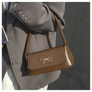 Détail du sac baguette en cuir mat marron avec nœud métallique porté à l'épaule
