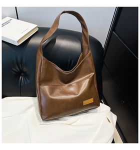 Brown leather tote bag displayed on a black leather sofa with artistic books as props