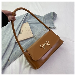 Détail du sac baguette en cuir caramel avec boucle noeud dorée sur une veste en jean bleu