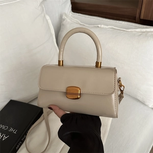 Elegant cream leather crossbody bag with gold buckle and top handle in a minimalist style
