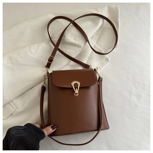 Detail of brown vintage bucket bag with golden teardrop clasp on striped shirt background