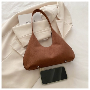 Détail du sac croissant en daim marron avec rivets argentés sur un blazer beige