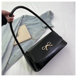 Détail du sac baguette en similicuir noir avec une boucle en métal doré en nœud
