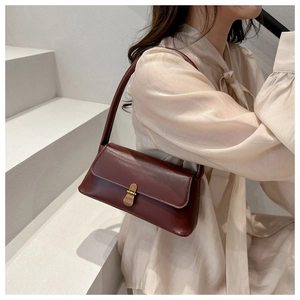 Detail of dark brown leather baguette bag with vintage gold buckle on a shoulder strap