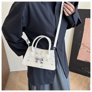 Detail of woven beige straw bag featuring a silver bow and delicate floral embroidery