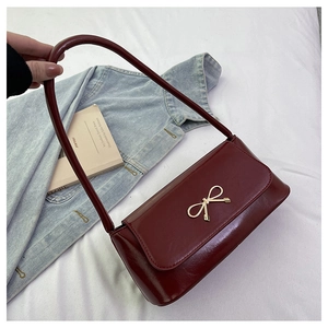 Détail d'un sac bandoulière rouge foncé avec boucle noeud dorée sur un drap blanc