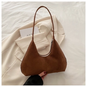 Détail d'un sac hobo en daim marron foncé posé sur un blazer blanc avec des livres