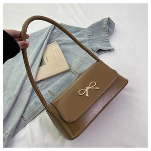 Détail du sac baguette en cuir marron avec nœud doré et fermeture à rabat chic