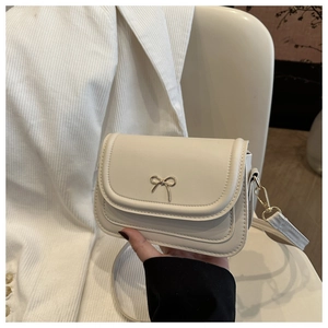 Detail of elegant beige crossbody bag featuring a decorative gold bow metal clasp