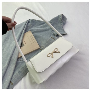 Détail d'un sac baguette blanc avec boucle noeud doré posé sur un tissu en jean
