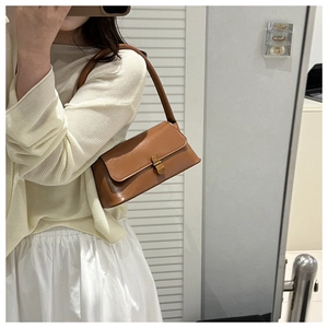 Close-up of brown glossy leather shoulder bag with a vintage gold rectangular metal buckle