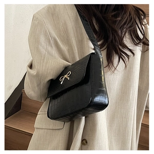 Détail du sac à bandoulière noir texture crocodile avec boucle dorée sur blazer en lin