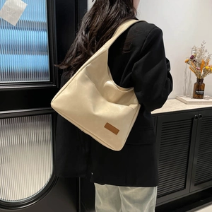 Minimalist beige tote bag in soft faux leather shown on shoulder in stylish room setting