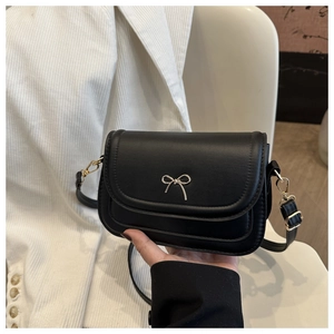 Detail of a black leather handbag featuring a decorative gold bow and adjustable strap