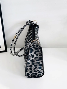 Detail of leopard print handbag showing knotted strap, metal zipper and textured surface