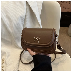 Detail of a brown small crossbody bag featuring a golden metal bow clasp and PU leather texture