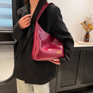 Glossy burgundy tote bag with shoulder strap in a minimalist interior setting