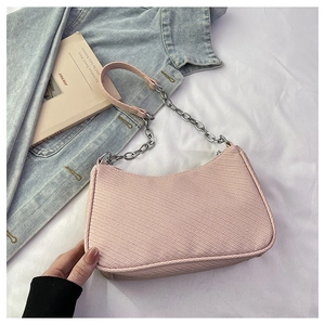 Detail of pink woven baguette bag with silver chain strap on a denim jacket backdrop