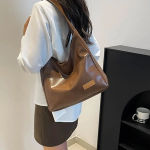 Brown high-gloss large capacity tote bag shown on model in minimalist interior setting