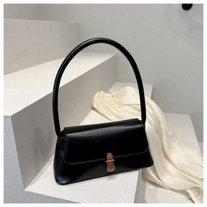 Minimalist black square shoulder bag with high-arched handle and brass buckle on white stairs